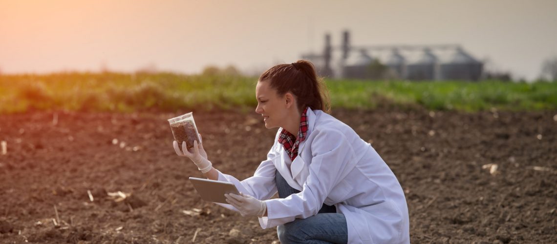 Young pretty woman agronomist checking soil quality on field